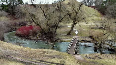 Low-angle-shot-of-a-narrow-wooden-bridge-crossing-a-green-river-in-a-forest