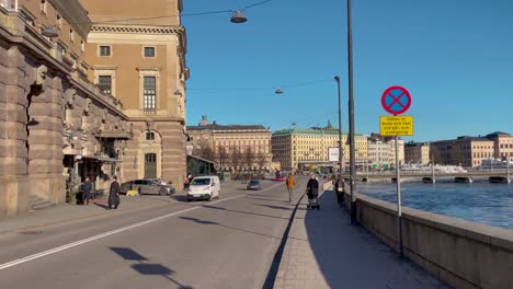 Sonniger-Tag-In-Stockholm-Mit-Royal-Opera-Und-Grand-Hotel,-Autos-Und-Fußgänger-Am-Wasser