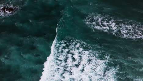 aerial-top-down-video-of-large-and-powerful-waves-crashing-down-on-the-rocky-shore-line-on-a-hot-and-sunny-day-by-the-coast-in-Hawaii