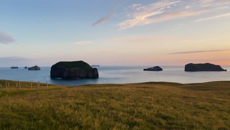 Golden-hour-seascape-with-serene-ocean-and-grassy-foreground-in-Iceland,-distant-islands,-tranquil-mood