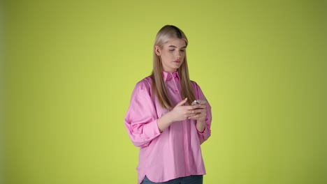 Woman-with-pink-shirt-typing-on-Cellphone,-studio-shot,-yellow-background