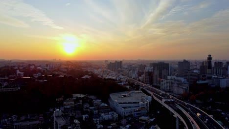 Sunset-skyline-view-of-a-bustling-city-with-golden-hues-and-busy-roads,-aerial-shot