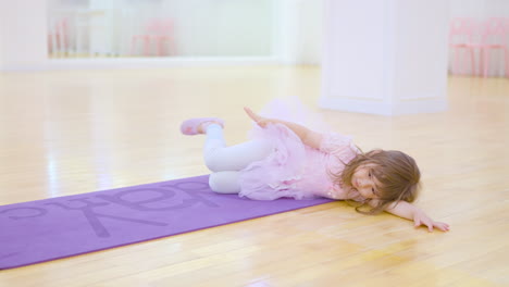 Adorable-Little-Ballerina-in-a-Pink-Tutu-Dress-Stretches-Practice-Ballet-Exercises-in-Studio-Lying-on-Floor