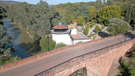 Vista-Aérea-Del-Puente-Del-Siglo-XVI-Que-Cruza-El-Río-Guadalquivir-Y-Atraviesa-Los-Edificios-Y-Jardines-Del-Balneario-De-Marmolejo,-Situado-En-La-Provincia-De-Jaén.