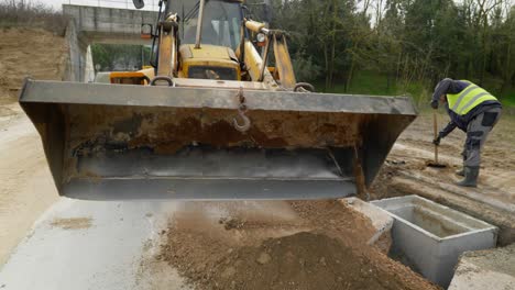 backhoe-loader-cleaning-road-from-gravel-on-new-drainage-pipe-system