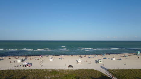 Aerial-View-of-South-Beach-on-Sunny-Day,-Miami-Florida-USA,-People-and-Cart-Vehicle-on-Sand,-Sliding-Drone-Shot