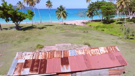 Cabaña-De-Hierro-Corrugado-Oxidado-En-Una-Playa-De-Arena-Tropical-En-El-Caribe,-Aérea