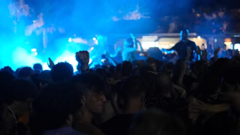 Slow-Motion-Static-Shot-of-Young-People-Throwing-Hands-Up-During-DJ-Set-with-Smoke---Blue-Light-Show