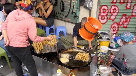 Busy-street-food-stall-in-Hanoi-frying-flatbreads,-bustling-atmosphere,-daylight