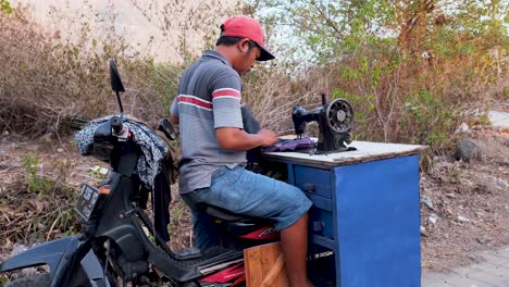 Man-sitting-on-a-scooter-on-an-attached-mobile-sewing-machine-and-sews-on-trousers