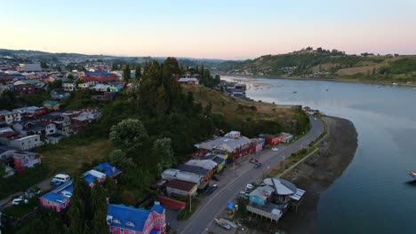 Aerial-view-of-Castro-winding-coastline,-Colorful-settlement-at-sunrise,-Ascending-shot,-Chile