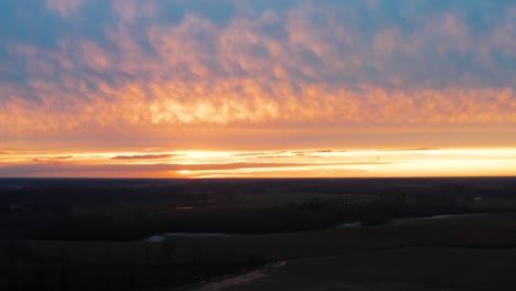 Flying-over-dark-countryside-field-during-vivid-golden-hour-sunset