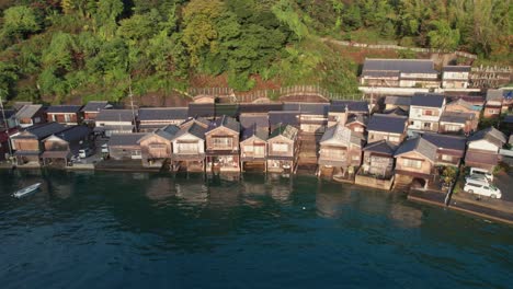 Aerial-drone-fly-above-stilt-houses,-Japanese-beach-water-shore-landscape-hills-with-green-trees,-turquoise-sea-in-Japan-Kyoto-Kyotango,-travel-destination-top-down-establishing-shot,-Asia