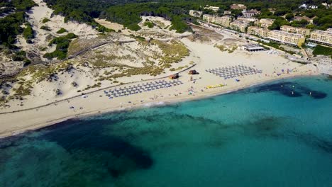 Panorámica-Con-Drones-De-Izquierda-A-Derecha-Del-Cuadro,-Delante-Y-Encima-De-La-Playa-De-Cala-Mesquida,-Un-Destino-Turístico-En-La-Isla-De-Mallorca-En-España.