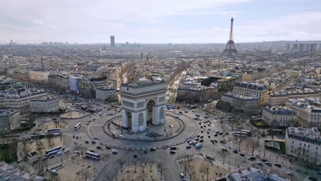 Triumphal-arch-and-car-traffic-on-roundabout-with-Tour-Eiffel-in-background,-Paris-cityscape,-France