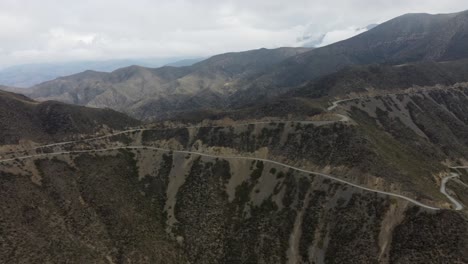 Aerial:-Serpentine-dirt-road-winds-down-mountain-pass-in-switchbacks