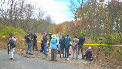 Un-Grupo-De-Personas-Se-Reunieron-En-La-Escena-Del-Crimen-En-El-Bosque-Durante-El-Día,-Algunas-Con-Cámaras