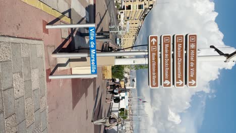 Ville-de-Marseille-sign-and-people-walking-in-sunlight,-vertical-shot