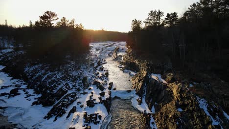 Atemberaubende-Aussicht-Auf-Den-Flussfall,-Umgeben-Von-Schnee-über-Felsigen-Felsen-In-Der-Goldenen-Stunde