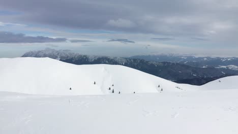 Snow-covered-slopes-with-skiers-in-the-Romanian-Carpathians,-Piatra-Craiului-in-the-backdrop