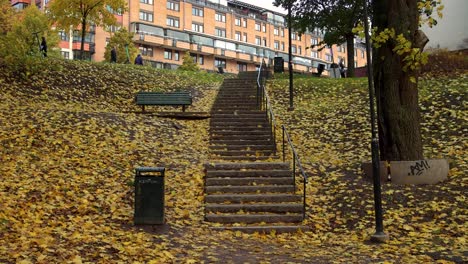 Herbstblätter-Fallen-An-Einer-Treppe-Im-Park,-Menschen-Bewegen-Sich-Im-Hintergrund