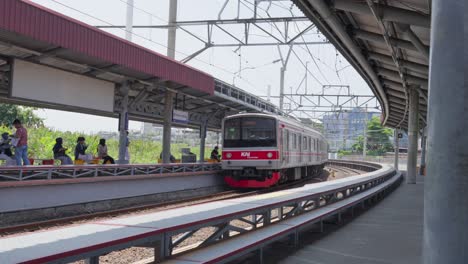 Zug-Kommt-Am-Bahnhof-Tangerang-Selatan-An,-Passagiere-Warten,-Sonniger-Tag,-Seitenansicht