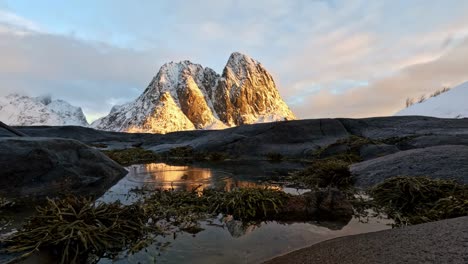 Olenils-island-and-Olstinden-in-Reine-Lofoten-at-sunset,-small-rings-moving-in-mirror-like-water
