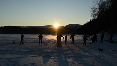 Friends-playing-ice-hockey-on-lake-during-beautiful-vibrant-sunset,-Norway-slow-motion