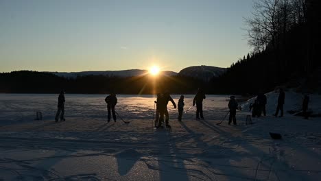 Amigos-Jugando-Hockey-Sobre-Hielo-En-El-Lago-Durante-La-Hermosa-Y-Vibrante-Puesta-De-Sol,-Noruega-En-Cámara-Lenta