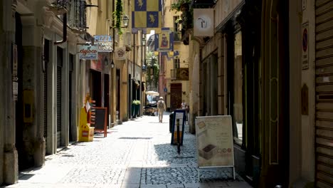 Downward-Tight-Pan-of-Colorful-Italian-Alley-with-Flags-Settling-on-Old-Man-Walking-Alone