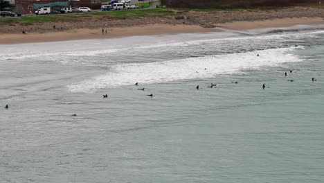 Drone-shot-panning-across-the-beachfront-with-waves-crashing-and-surfers-waiting