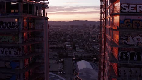 Close-up-reverse-pullback-aerial-shot-of-the-unique-graffiti-murals-on-the-balcony-windows-of-the-abandoned-Oceanwide-Plaza-skyscrapers-in-downtown-Los-Angeles,-California-at-sunset