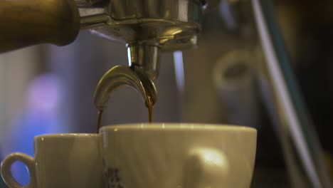 Coffee-Pouring-into-Two-Cups-in-a-Coffee-Shop-in-the-Morning,-People-Walking-on-Background,-Close-Up