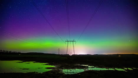 Magnetic-space-storm-above-a-pylon-and-wet,-reflecting-farmlands---Time-lapse-shot