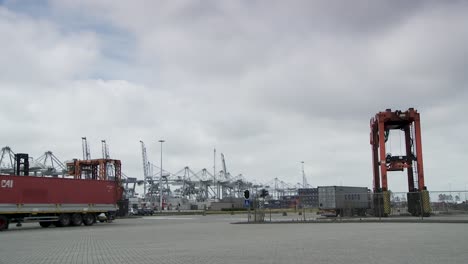 Bewölkter-Tag-An-Einem-Geschäftigen-Containerterminal-Mit-Lastwagen-Und-Kränen,-Bedeckter-Himmel