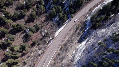 A-car-drives-along-a-road-on-a-snowy-mountain,-drone-aerial-top-down-view