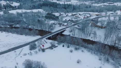 Paisaje-Cubierto-De-Nieve-Del-Pueblo-De-Renda-Del-Río-Abava,-Vista-Aérea,-Sereno-Día-De-Invierno,-Avanzando,-Inclinado-Hacia-Abajo