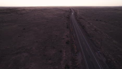 Distant-cars-driving-down-a-remote-desert-highway-at-sunset