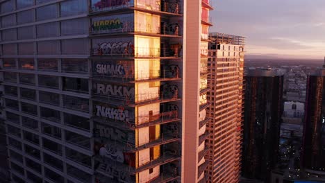 Close-up-descending-and-panning-aerial-shot-of-the-Oceanwide-Plaza-graffiti-towers-in-downtown-Los-Angeles,-California-at-sunset