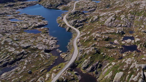 Aerial-shot,-panning-across-a-winding-mountain-road-as-it-snakes-through-the-mossy,-rocky,-lake-covered-landscape-of-Rogaland-in-Norway