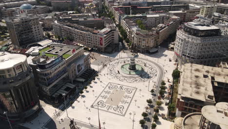 Vista-Aérea-De-La-Plaza-Macedonia,-Skopje,-Los-Edificios-Del-Centro,-El-Gran-Monumento-De-Alejandro-Y-La-Gente-En-Un-Día-Soleado---Estableciendo-Un-Disparo-Con-Drones