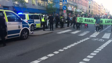 Pan-from-police-car-to-protesters-with-banner-at-demonstration,-Sweden