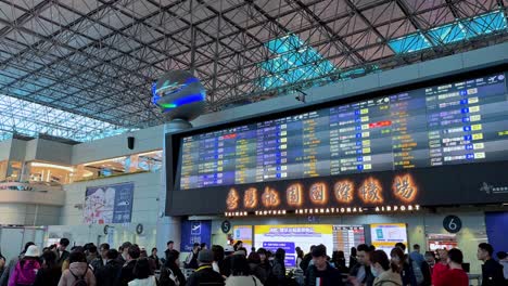 Concurrido-Aeropuerto-Internacional-De-Taiwán-Taoyuan-Con-Viajeros-Y-Pantallas-De-Información-De-Vuelos,-Toma-Interior-A-La-Luz-Del-Día