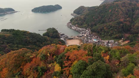 Aerial-drone-autumn-forest-hill-landscape-above-Japanese-Kyotango-bay-beach-town-travel-destination-in-Kyoto,-Japan,-colorful-trees-and-house-village-near-the-Sea-travel-islands