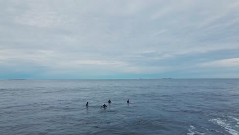 Aerial-flyover-group-of-surfer-sitting-on-board-in-ocean-during-cloudy-day