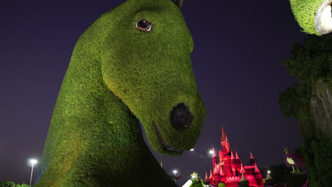 Miracle-Garden-Dubai,-Escultura-De-Caballo-Verde-Y-Pequeño-Castillo-Iluminado-Por-La-Noche