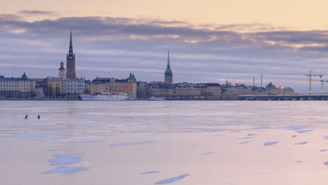 Vista-De-Camiones-Con-Drones-Sobre-El-Lago-Helado-Malaren-Con-Vistas-De-Gamla-Stan-Y-Slussbron