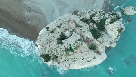 Aerial-top-down-view-of-the-famous-Aphrodite's-Rock-surrounded-by-turquoise-waters-and-a-sandy-beach-in-Cyprus