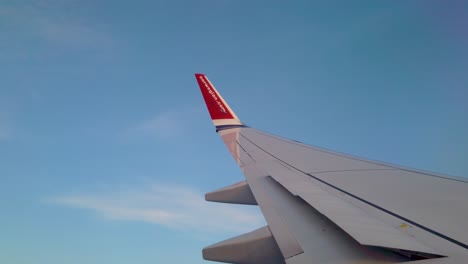 Wing-of-Norwegian-airlines-plane-as-it-turns-in-blue-sky,-POV