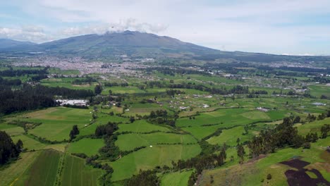 Cinematic-drone-clip-moving-over-the-green-fields-towards-a-small-town-under-a-mountain-in-Puichig,-Equador